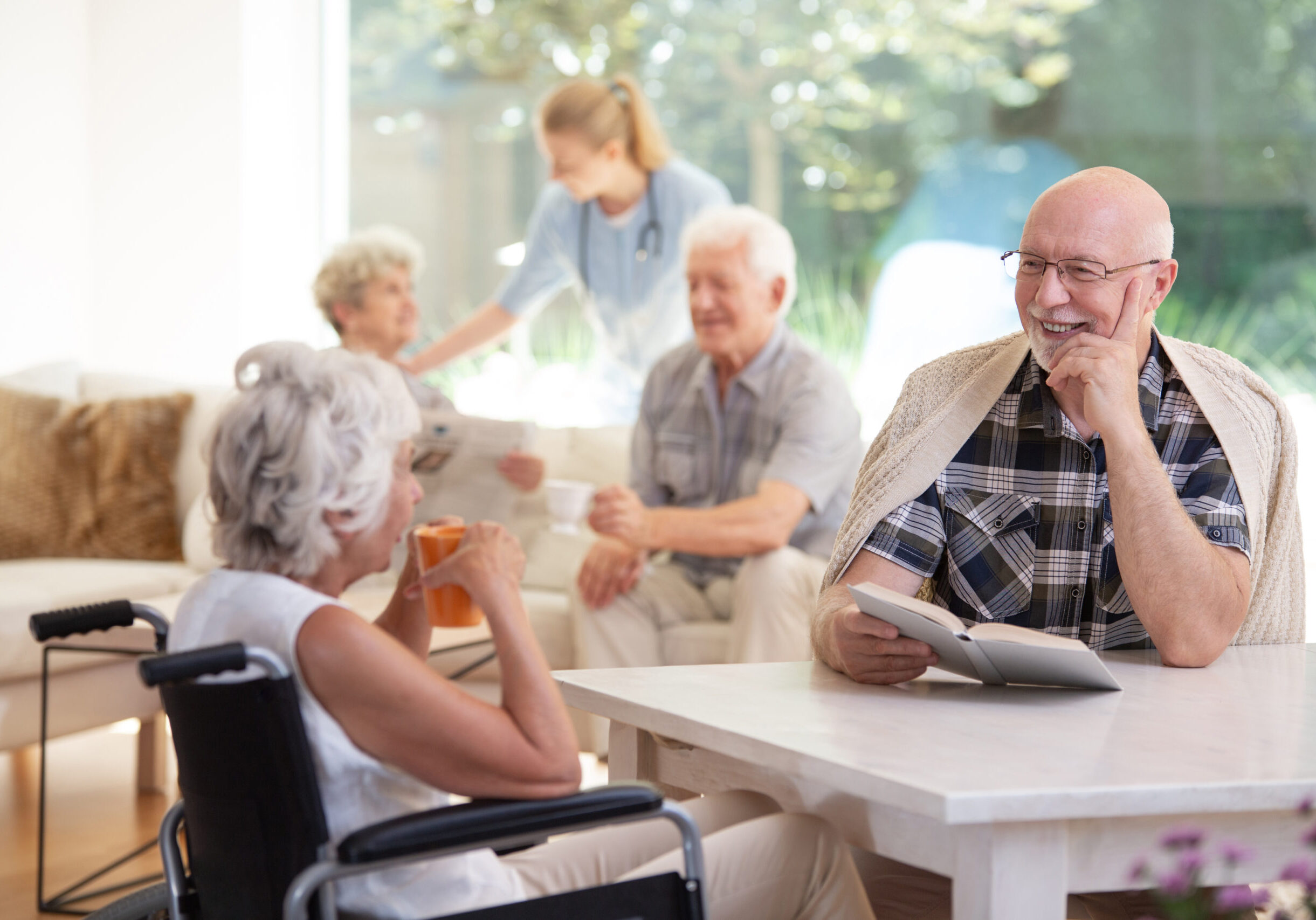 Elderly woman in the wheelchair drinking tea during conversation with smiling friend