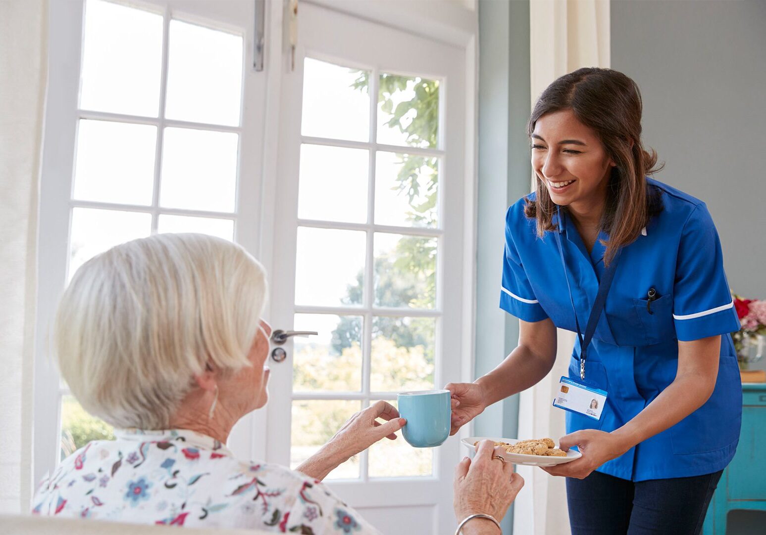 Nurse providing elderly women with tea and cakes